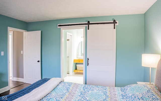 bedroom with a barn door, ensuite bathroom, and hardwood / wood-style flooring