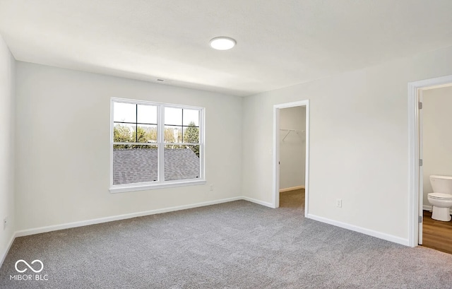 unfurnished bedroom with light carpet, ensuite bath, a closet, and a walk in closet