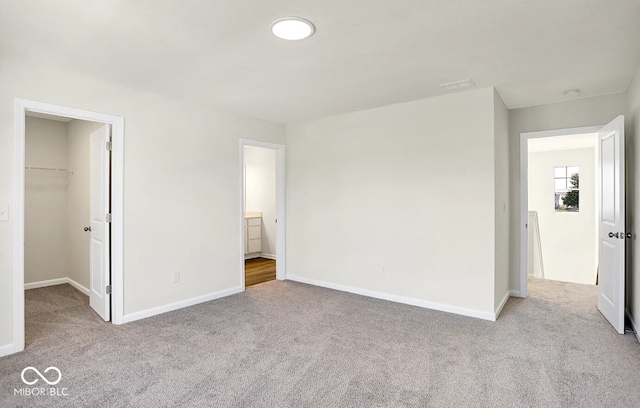 unfurnished bedroom with ensuite bathroom, a spacious closet, light colored carpet, and a closet