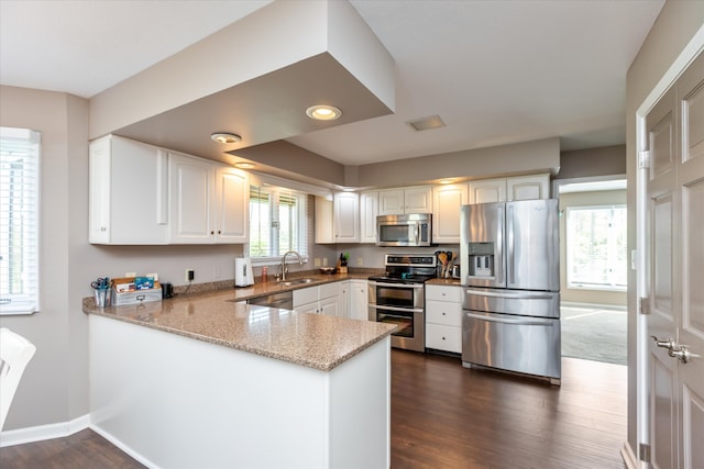 kitchen with white cabinetry, dark hardwood / wood-style floors, kitchen peninsula, stainless steel appliances, and light stone counters