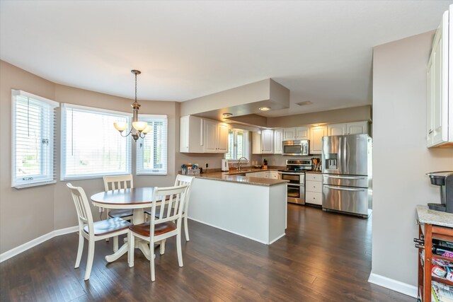 kitchen featuring kitchen peninsula, decorative light fixtures, stainless steel appliances, dark hardwood / wood-style floors, and sink