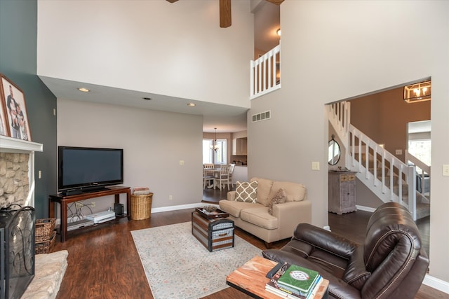 living room featuring an inviting chandelier, a stone fireplace, a towering ceiling, and dark wood-type flooring