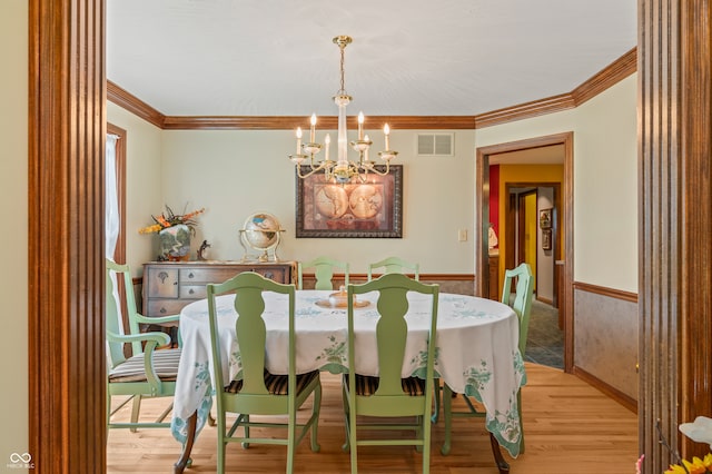 dining space with crown molding, an inviting chandelier, and light hardwood / wood-style flooring