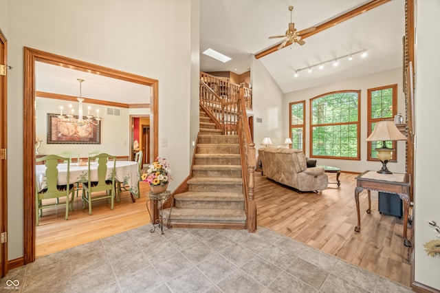 stairs with high vaulted ceiling, track lighting, hardwood / wood-style flooring, and ceiling fan with notable chandelier