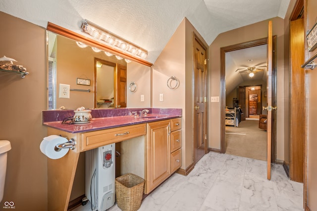 bathroom featuring vaulted ceiling, toilet, ceiling fan, large vanity, and a textured ceiling