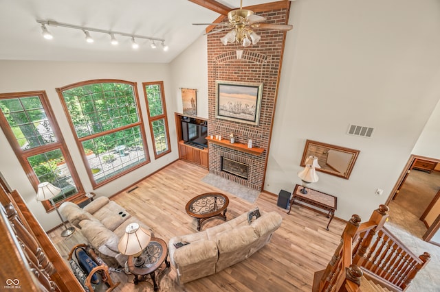 living room with brick wall, a brick fireplace, ceiling fan, rail lighting, and high vaulted ceiling