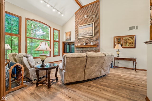 living room with high vaulted ceiling, brick wall, hardwood / wood-style flooring, and rail lighting