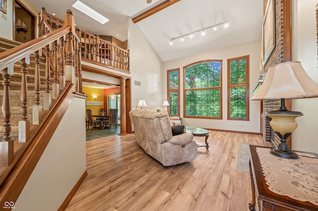 living room with high vaulted ceiling, wood-type flooring, track lighting, and a skylight