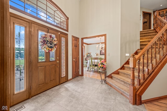 foyer featuring a towering ceiling, an inviting chandelier, and light tile flooring