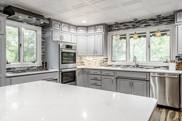 kitchen featuring gray cabinetry, wall chimney range hood, sink, light stone counters, and stainless steel appliances