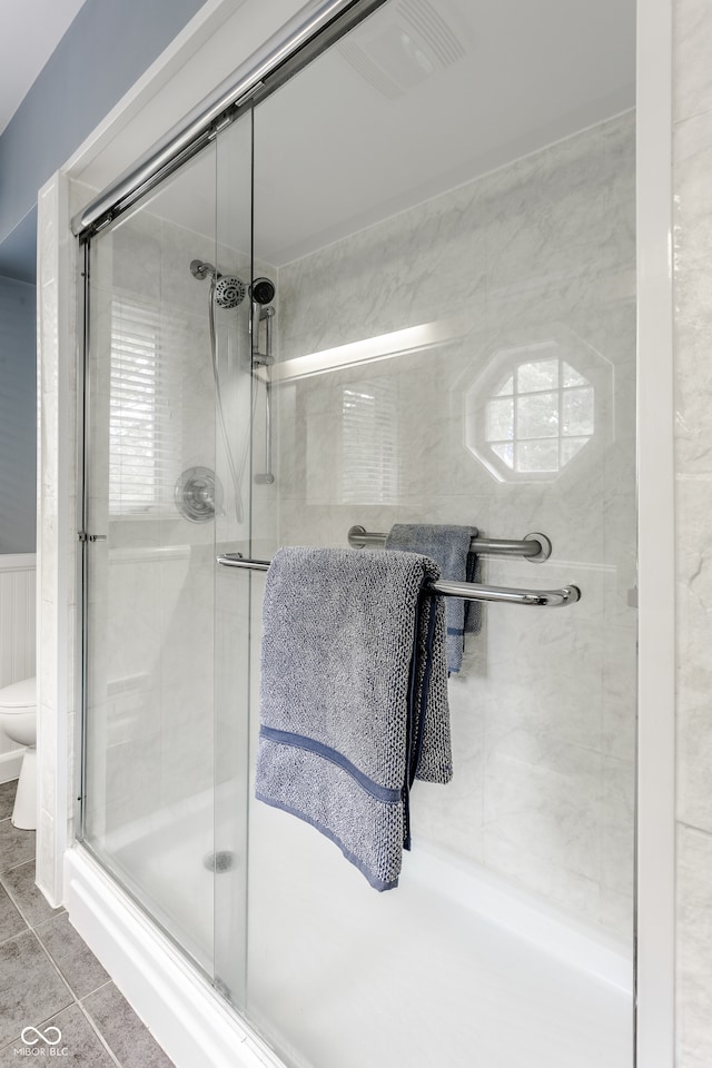 bathroom featuring tile patterned flooring, toilet, and a shower with door