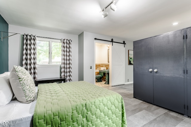 bedroom with a barn door, rail lighting, and ensuite bath