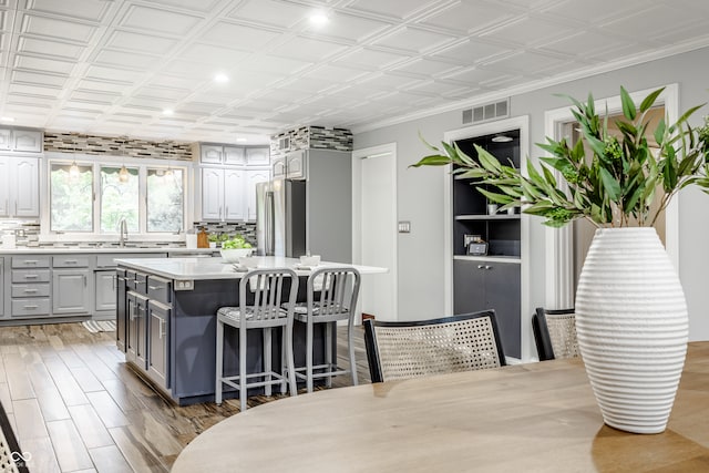 kitchen featuring gray cabinetry, sink, stainless steel fridge, a kitchen island, and a breakfast bar area