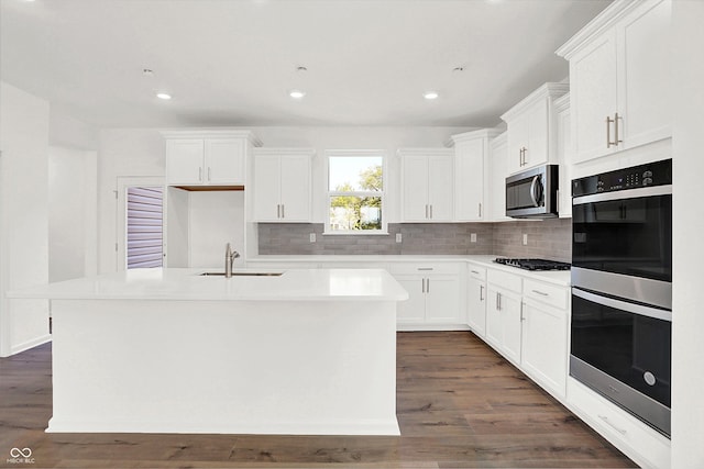 kitchen featuring appliances with stainless steel finishes, white cabinetry, sink, dark hardwood / wood-style floors, and a center island with sink