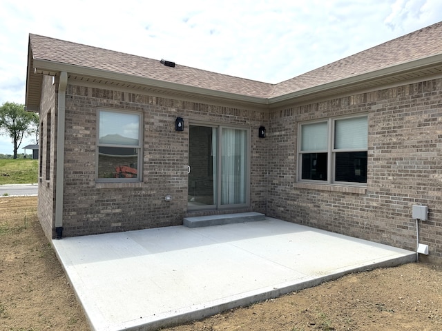 exterior space with a shingled roof, a patio area, and brick siding