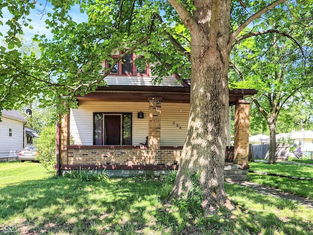 view of front of house with covered porch, brick siding, fence, and a front lawn