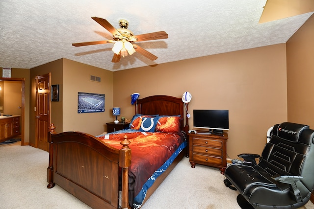 bedroom with a textured ceiling, ensuite bathroom, ceiling fan, and light colored carpet