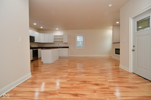 547 Udell St, Indianapolis, IN 46208 - unfurnished living room featuring light wood finished floors, recessed lighting, a glass covered fireplace, baseboards, and a sink