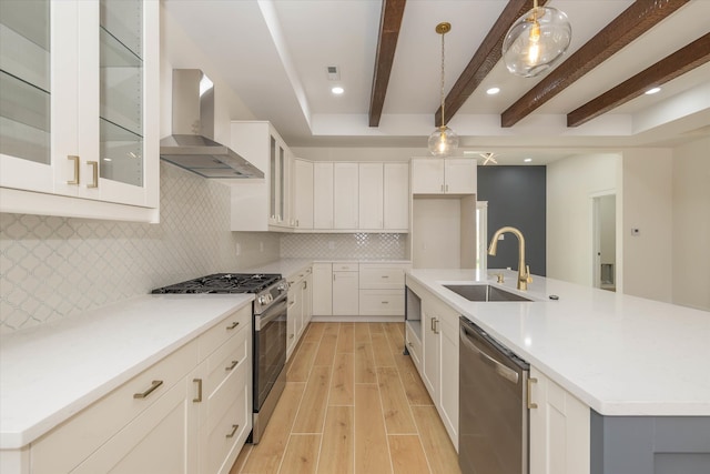 kitchen featuring wall chimney exhaust hood, hanging light fixtures, stainless steel appliances, a center island with sink, and sink