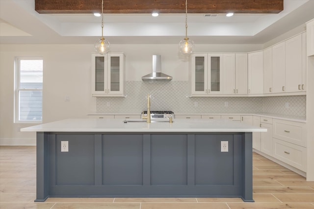 kitchen with white cabinets, hanging light fixtures, wall chimney range hood, and a kitchen island with sink