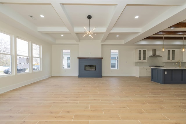 unfurnished living room featuring coffered ceiling, light hardwood / wood-style floors, a chandelier, and sink