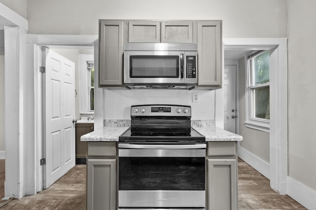 kitchen with appliances with stainless steel finishes, gray cabinets, tasteful backsplash, light stone counters, and dark hardwood / wood-style flooring