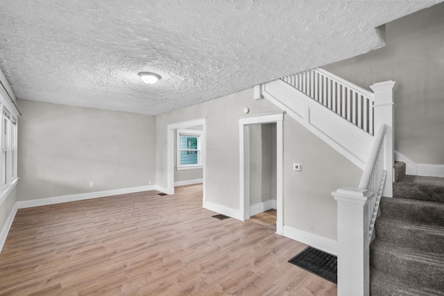 stairway with a textured ceiling and light wood-type flooring