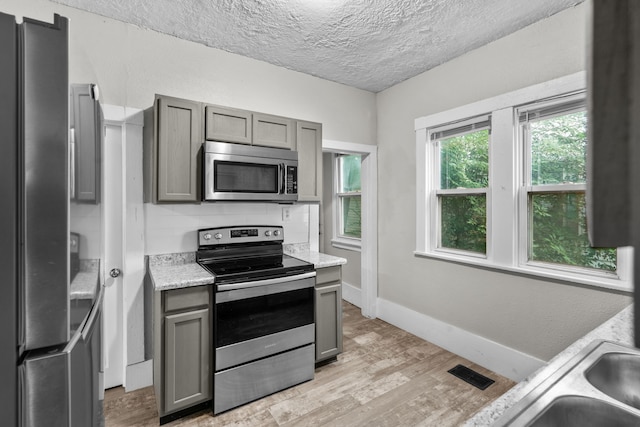 kitchen with gray cabinetry, stainless steel appliances, light hardwood / wood-style floors, and light stone counters