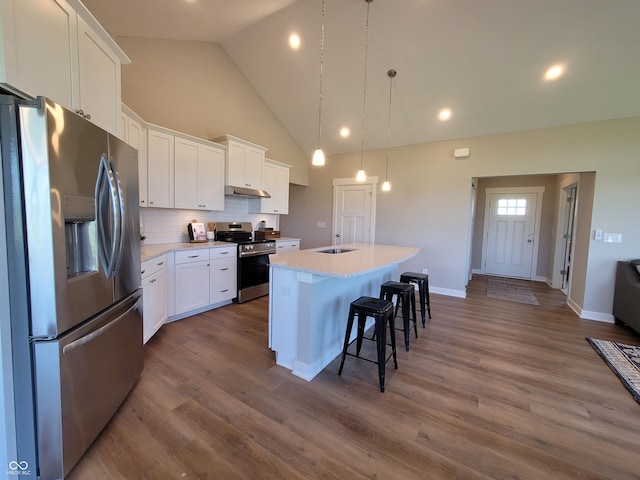 kitchen with white cabinets, stainless steel appliances, hanging light fixtures, and an island with sink