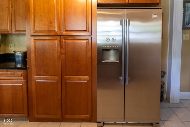 kitchen with stainless steel refrigerator with ice dispenser, light tile patterned floors, and dark stone countertops