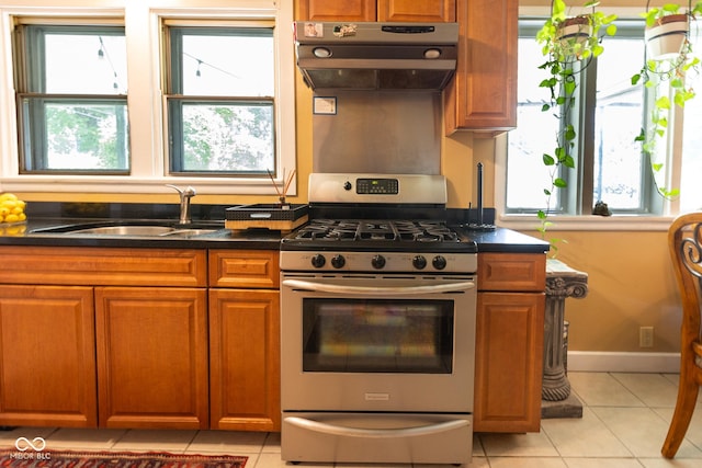 kitchen featuring stainless steel gas range oven, sink, light tile patterned floors, and extractor fan