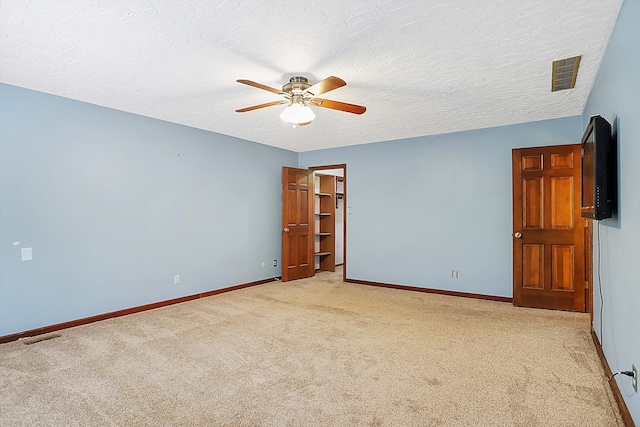 spare room featuring light carpet, ceiling fan, and a textured ceiling