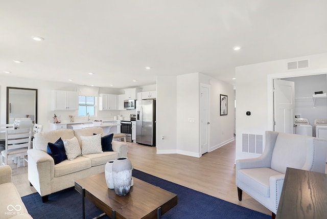 living room featuring washing machine and dryer, light hardwood / wood-style floors, and sink