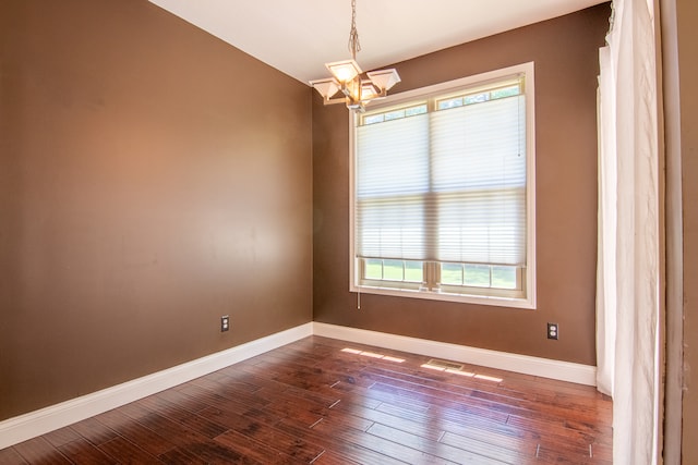 spare room with plenty of natural light, a chandelier, and dark wood-type flooring