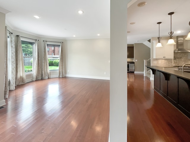 kitchen featuring dark hardwood / wood-style floors, decorative light fixtures, backsplash, wall chimney exhaust hood, and white cabinetry