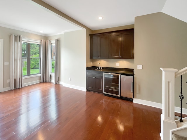 bar with dark brown cabinets, hardwood / wood-style floors, ornate columns, wine cooler, and sink