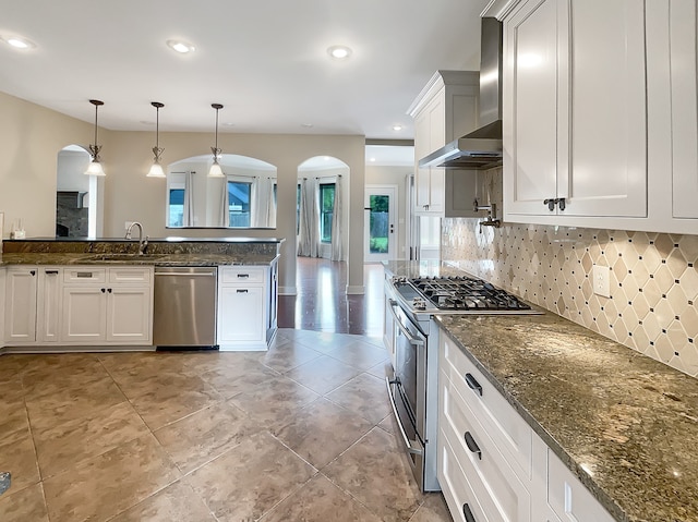 kitchen with stainless steel appliances, backsplash, wall chimney exhaust hood, white cabinets, and pendant lighting