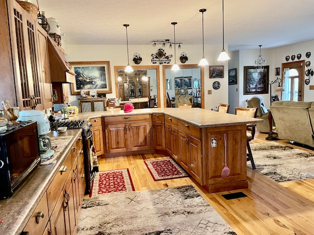 kitchen featuring decorative light fixtures, stainless steel gas range oven, a breakfast bar area, and light hardwood / wood-style flooring