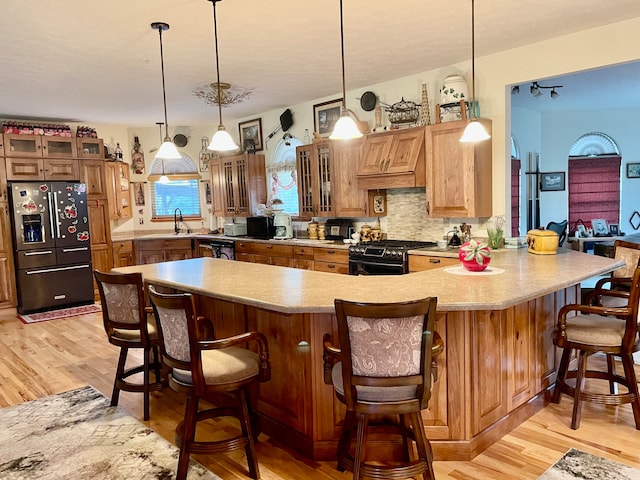 kitchen with a kitchen bar, stainless steel refrigerator with ice dispenser, backsplash, black gas range oven, and light hardwood / wood-style flooring