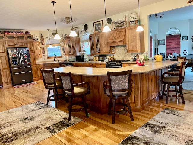 kitchen with light hardwood / wood-style floors, black range with gas cooktop, a breakfast bar area, and fridge with ice dispenser