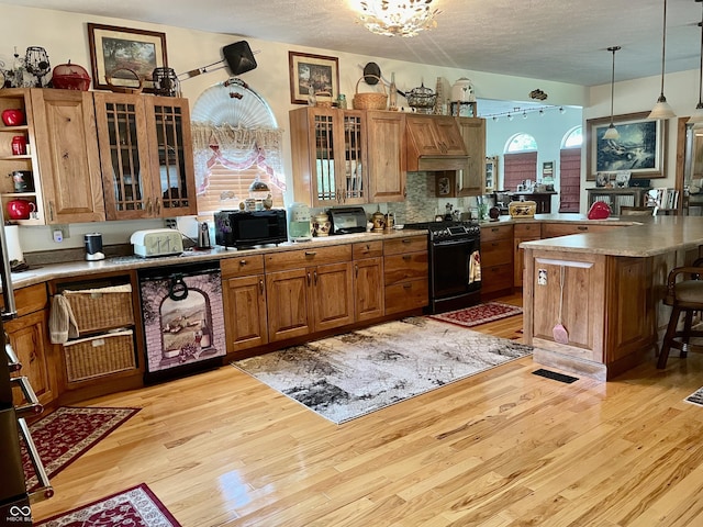 kitchen featuring a kitchen breakfast bar, light hardwood / wood-style floors, hanging light fixtures, and black appliances