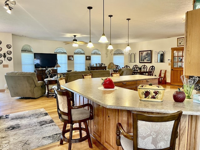 kitchen with pendant lighting, a breakfast bar, light hardwood / wood-style floors, and ceiling fan with notable chandelier