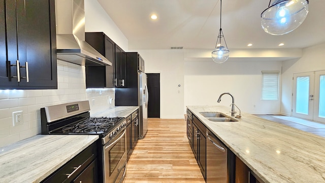 kitchen with pendant lighting, wall chimney range hood, sink, tasteful backsplash, and stainless steel appliances