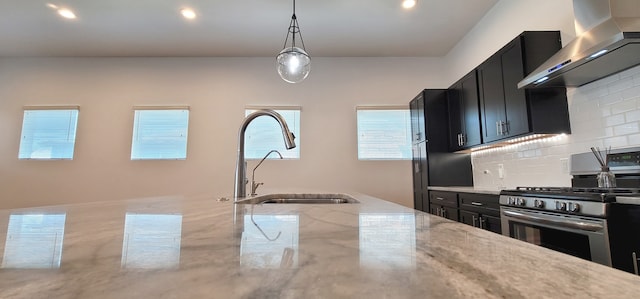 kitchen with sink, wall chimney range hood, stainless steel gas range oven, backsplash, and pendant lighting