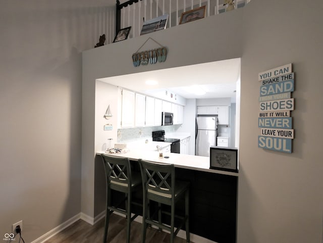 kitchen featuring a kitchen bar, stainless steel appliances, dark wood-type flooring, kitchen peninsula, and white cabinetry