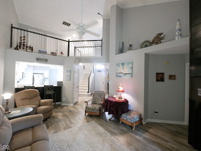 living room with a high ceiling, hardwood / wood-style floors, ceiling fan, and crown molding