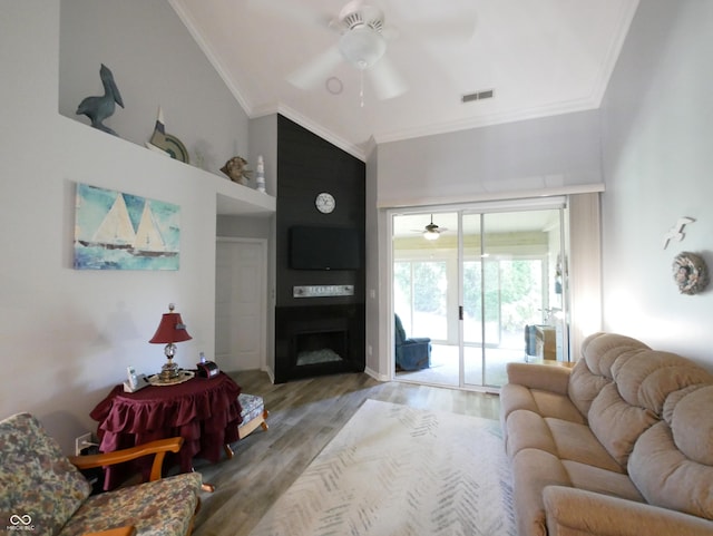 living room with vaulted ceiling, hardwood / wood-style floors, ornamental molding, ceiling fan, and a large fireplace