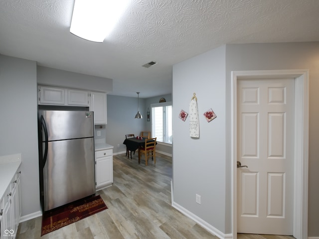 kitchen featuring hanging light fixtures, a textured ceiling, white cabinetry, light wood-type flooring, and stainless steel fridge