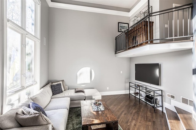 living room featuring dark wood-type flooring, a towering ceiling, and ornamental molding