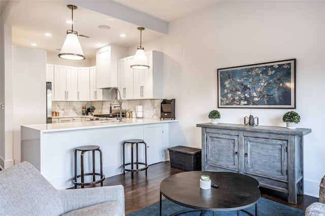 kitchen featuring kitchen peninsula, hanging light fixtures, tasteful backsplash, dark wood-type flooring, and white cabinets